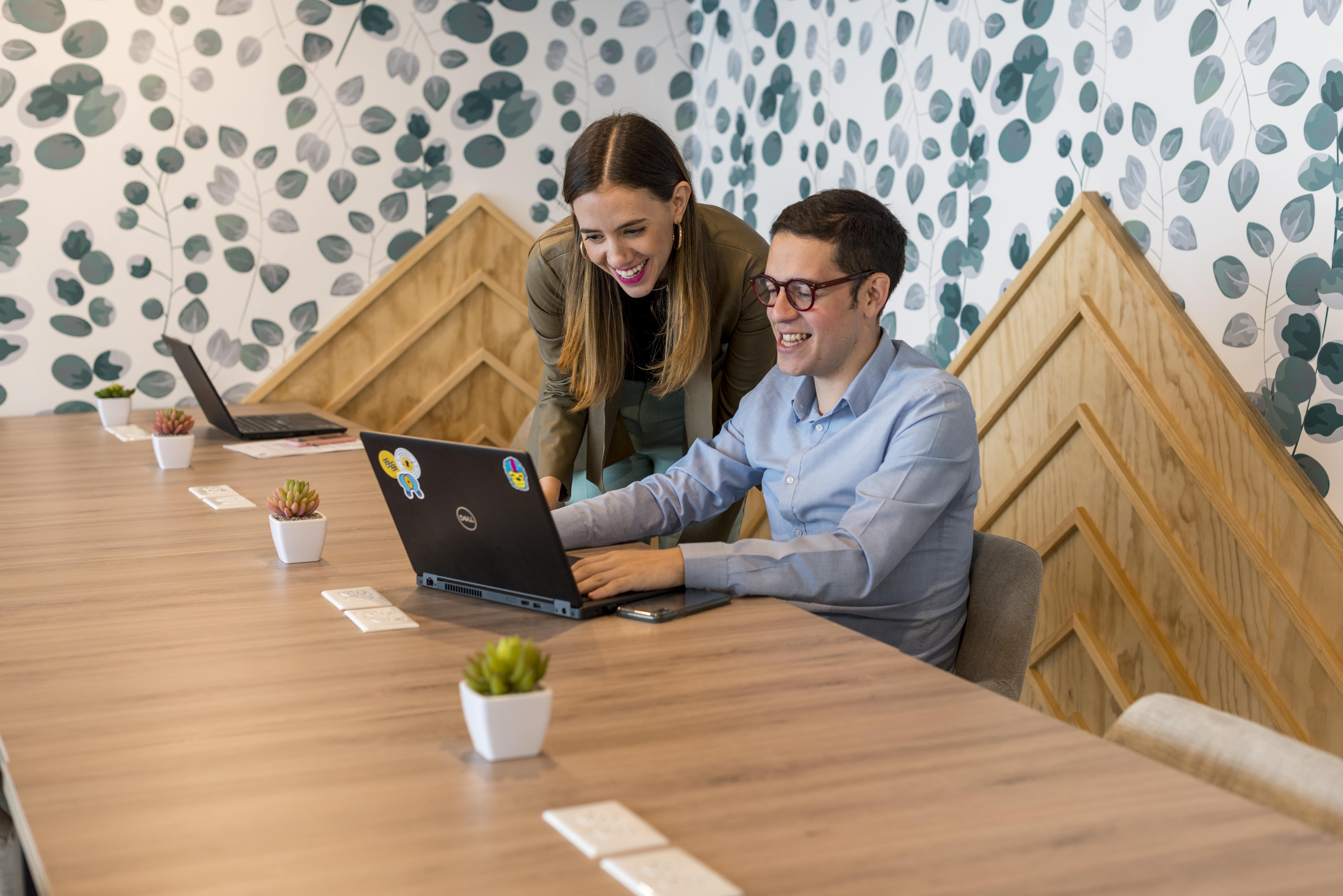 dos sonrientes colaboradores revisando una laptop en una oficina
